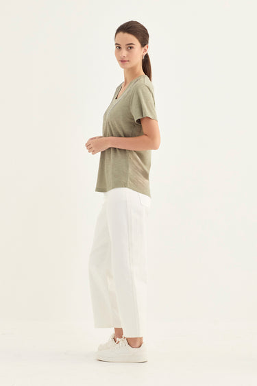 A woman modeling a short-sleeve olive green t-shirt and white wide-leg cropped pants by Verge, standing against a plain white studio background.