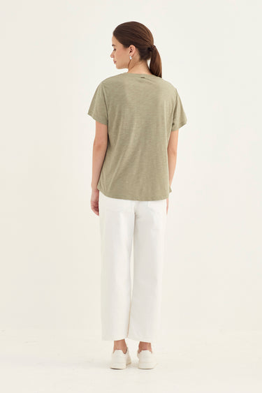 A woman shown from the back wearing a short-sleeve olive green t-shirt and white cropped pants by Verge, standing against a plain white studio background.