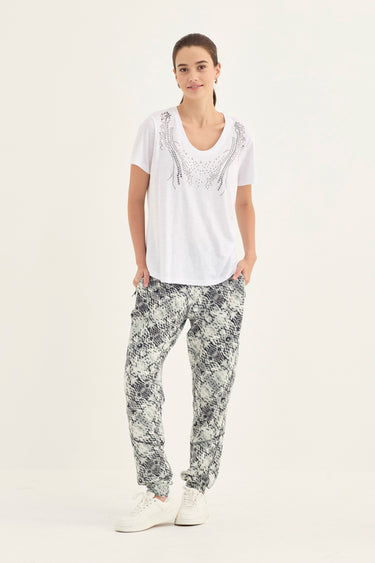 A woman modeling a white short-sleeve top with silver embellishments and black-and-white snakeskin print pants by Verge, standing against a plain white studio background.
