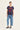 A woman modeling a dark navy blue graphic t-shirt with red cherry and text print, paired with light blue jeans by Verge and black flats, against a plain off-white studio background.