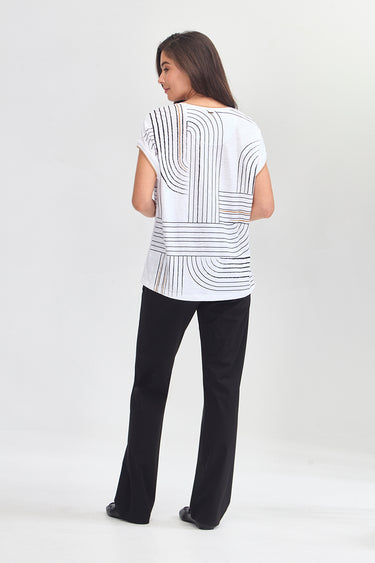 A woman shown from the back wearing a white short-sleeve top with a black geometric stripe pattern and black pants by Verge, standing against a light gray studio background.