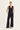 A woman modeling a black sleeveless vest with a button front and matching wide-leg pants by Verge, standing against a plain light background.