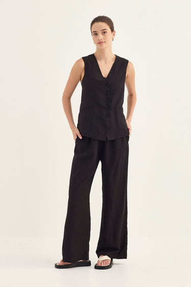 A woman modeling a black sleeveless vest with a button front and matching wide-leg pants by Verge, standing against a plain light background.