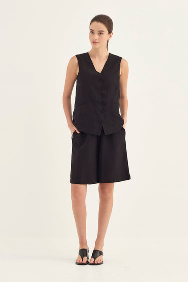 A woman modeling a black sleeveless button-front vest with matching black shorts by Verge against a plain light background.