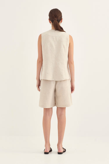 A woman viewed from the back wearing a light beige sleeveless linen vest and matching shorts by Verge, paired with black flat sandals, against a plain off-white studio background.