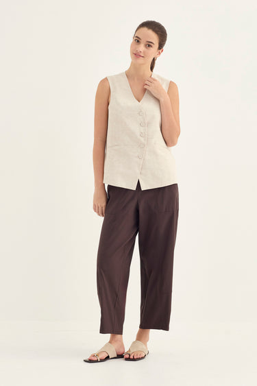 A woman modeling a sleeveless cream linen vest and dark brown wide-leg cropped pants by Verge against a plain off-white studio background.