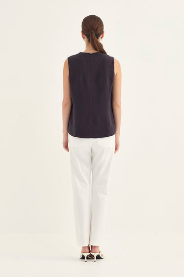 A woman viewed from the back wearing a sleeveless dark plum top and white trousers by Verge, standing against a plain light background.