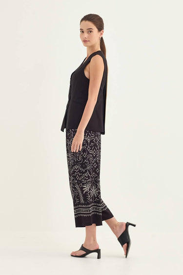 A woman modeling a sleeveless black peplum top and black-and-white patterned cropped pants by Verge with black heeled sandals, photographed against a plain light background.