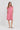 A woman modeling a short-sleeve pink linen dress by Verge with a split neckline and side pockets, standing against a plain white studio background.