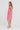 A woman modeling a short-sleeve pink linen dress with side pockets, standing in profile against a plain white studio background.