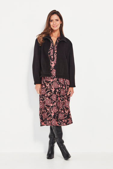 Woman wearing a black coat over a pink floral dress with black boots by Verge on a white background