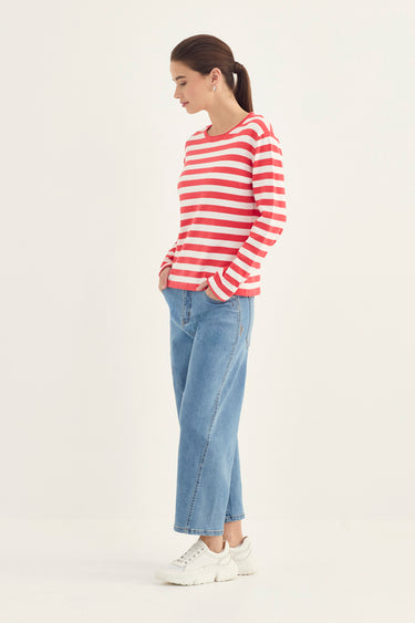 A woman modeling a red and white horizontally striped long-sleeve knit top, paired with light blue cropped jeans by Verge and white sneakers, standing against a plain off-white studio background.