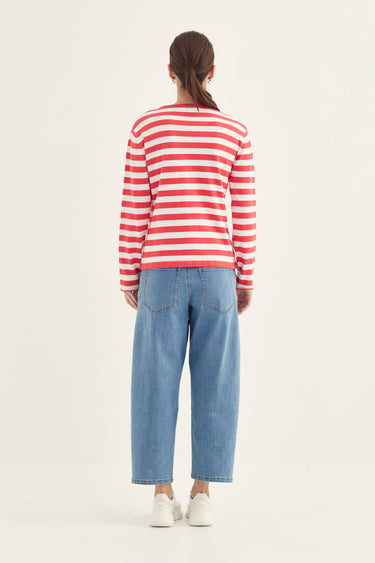 A woman viewed from behind wearing a red and white horizontally striped long-sleeve top, light blue wide-leg jeans by Verge, and white sneakers against a plain light background.