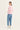 A woman shown from the back wearing a pink and white striped long-sleeve top, light blue cropped jeans by Verge, and white sneakers, standing against a plain off-white studio background.