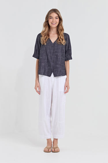 A woman modeling a short-sleeve dark gray textured linen blouse paired with white wide-leg cropped pants by Verge and tan sandals, standing against a light gray studio background.