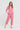 A woman modeling a pink two-piece linen pajama set consisting of a short-sleeve button-up top and matching cropped pants by Verge, photographed against a plain white studio background.
