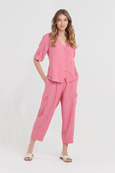 A woman modeling a pink two-piece linen pajama set consisting of a short-sleeve button-up top and matching cropped pants by Verge, photographed against a plain white studio background.