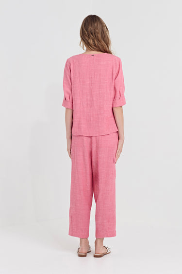 A woman viewed from the back wearing a matching pink two-piece outfit consisting of a short-sleeve cropped top and wide-leg cropped pants by Verge, paired with tan sandals, against a plain light gray studio background.