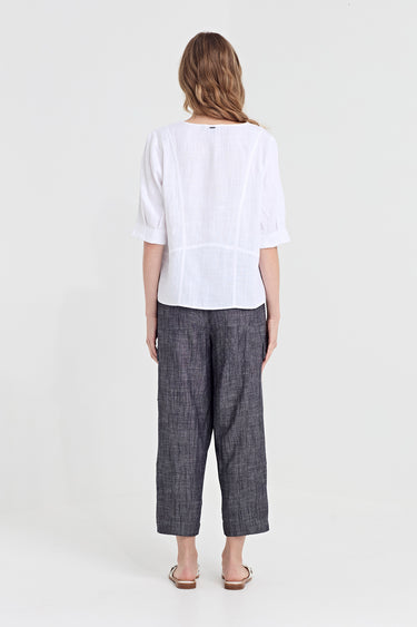 A woman viewed from the back wearing a white short-sleeve blouse and dark gray wide-leg cropped trousers by Verge, standing against a plain light gray studio background.