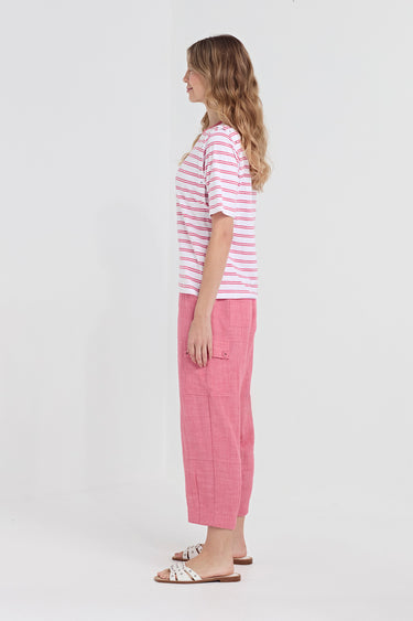 A woman stands in profile wearing a pink and white striped short-sleeve top, pink wide-leg cropped pants by Verge, and white slide sandals with brown straps, against a plain light gray studio background.