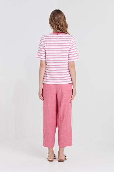 A woman viewed from the back wearing a pink and white striped short-sleeve t-shirt and pink cropped trousers by Verge, standing against a light gray studio background.