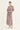 A woman modeling a long-sleeved maxi dress with a dusty rose and beige paisley pattern by Verge, standing against a plain off-white studio background.