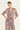 A woman modeling a long-sleeve midi dress with a dusty rose and beige paisley pattern, featuring a ruffled V-neckline and a matching fabric tie belt at the waist by Verge, set against a plain light background.