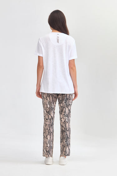 A woman shown from the back wearing a white short-sleeve t-shirt and beige and black snakeskin print pants by Verge, standing against a light gray studio background.