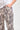 Close-up of a person wearing pants by Verge with a beige, brown, and black snakeskin pattern, paired with a white top against a light gray background.