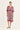 A woman modeling a short-sleeve V-neck kaftan dress by Verge with a red and purple circular pattern on a cream background, set against a plain off-white studio backdrop.