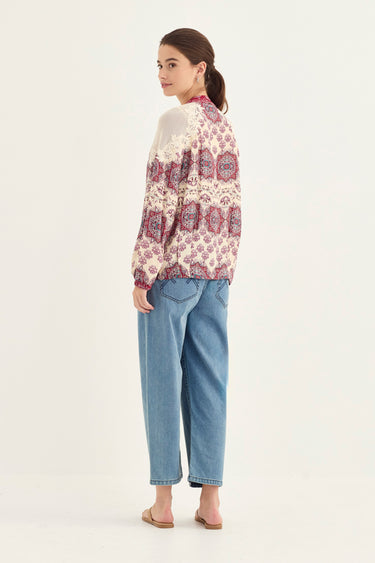 A woman is shown from the back wearing a cream-colored long-sleeve cardigan with a red and purple paisley pattern, paired with light blue cropped jeans by Verge and beige flat sandals, against a plain white studio background.
