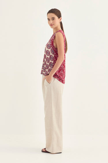 A woman modeling a sleeveless top with a red and purple paisley pattern, paired with off-white wide-leg trousers by Verge, photographed against a plain white studio background.