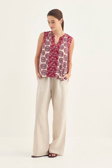 A woman modeling a sleeveless V-neck top with a red and purple floral pattern on a cream background, paired with wide-leg beige trousers by Verge, against a plain white studio background.