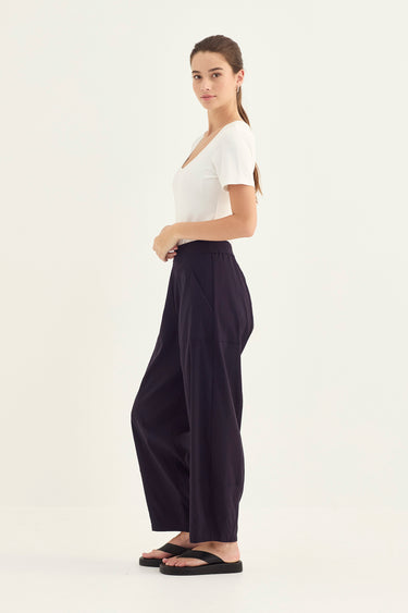 Woman wearing a white top and Midnight Homeland Pants by Verge on a white background