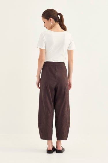 Woman wearing a white top and Chocolate Homeland Pants by Verge on a white background