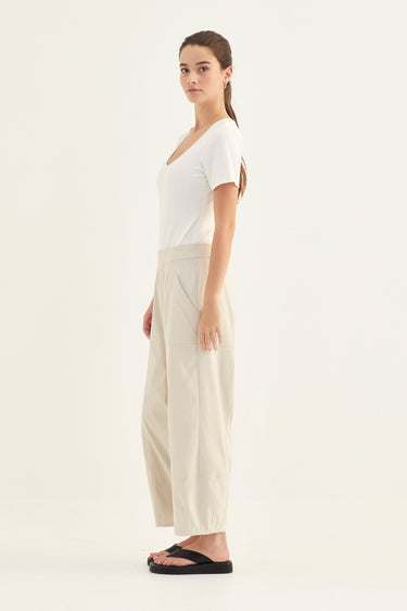 Woman wearing a white top and Putty Homeland Pants by Verge on a white background