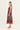 A woman modeling a sleeveless midi dress by Verge with a multicolor paisley pattern in shades of purple, blue, and orange, featuring a solid rust-red sheer overlay at the hem, set against a plain off-white studio background.