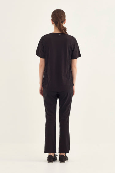 A model viewed from the back wearing a black short-sleeve crewneck t-shirt and matching black wide-leg pants by Verge, standing against a plain off-white studio background.