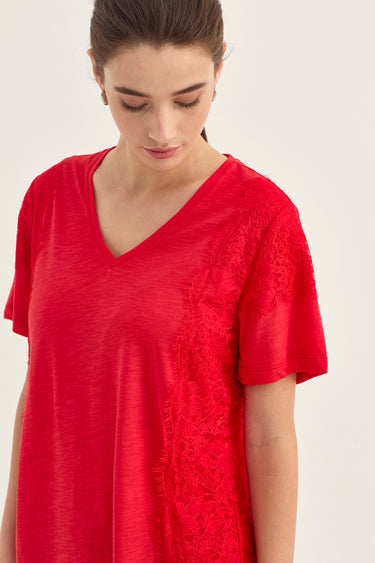 Close-up of a model wearing a red short-sleeve top by Verge with black lace applique panels along the shoulder and side, against a plain light background.