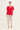 A woman modeling a bright red short-sleeve V-neck top paired with light beige wide-leg cropped pants by Verge and flat sandals, standing against a plain off-white studio background.