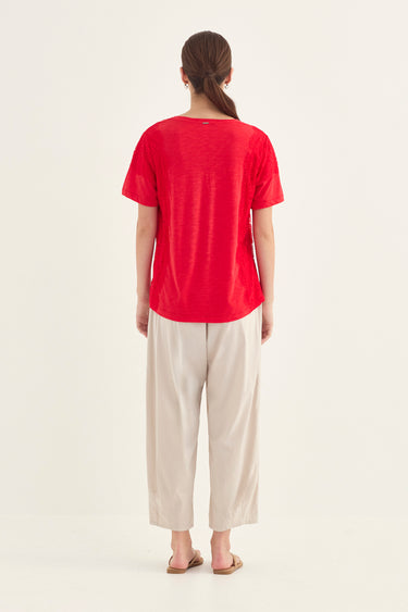 A woman viewed from behind, wearing a dark navy short-sleeve t-shirt and a pumice pant by Verge, standing against a plain off-white studio background.