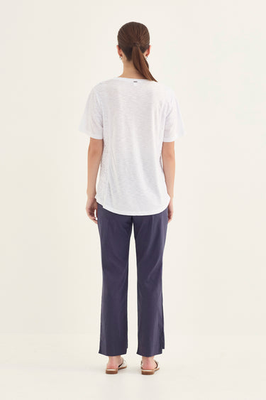 A woman viewed from the back wearing a white short-sleeve t-shirt and navy blue wide-leg pants by Verge, standing against a plain off-white studio background.