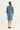 A woman viewed from the back wearing a light blue long-sleeve shirt dress by Verge with gathered sleeves and a straight knee-length hem, standing against a plain off-white studio background.