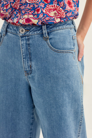 Close-up of a person wearing light blue denim jeans by Verge with a floral-patterned top partially visible at the waist.