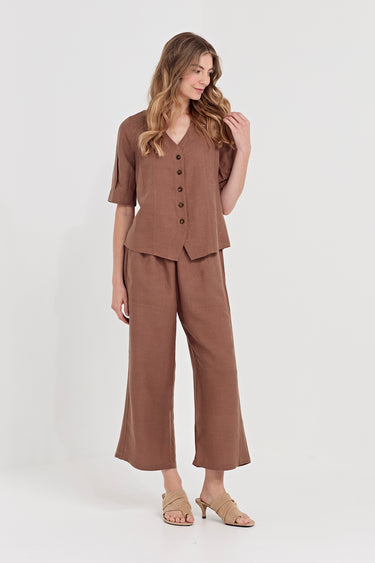 A woman modeling a matching two-piece linen set in a warm brown color, featuring a short-sleeve button-front top and wide-leg cropped pants by Verge, paired with beige heeled sandals against a plain white studio background.