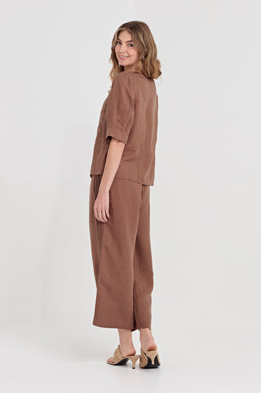 A woman modeling a matching two-piece brown outfit consisting of a short-sleeve cropped top and wide-leg cropped pants by Verge, paired with beige heeled sandals, against a plain light gray studio background.