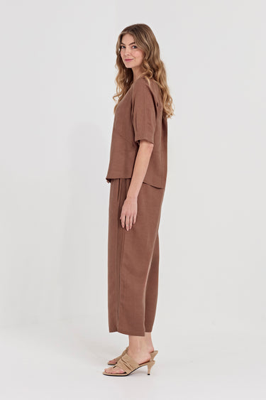A woman modeling a matching brown two-piece set consisting of a short-sleeve cropped top and wide-leg cropped pants by Verge, paired with beige heeled sandals, against a plain light gray studio background.