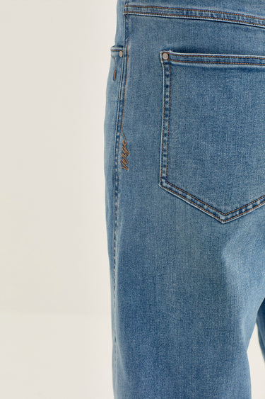 Close-up of the back pocket area of light blue denim jeans by Verge, showing the pocket stitching and a small embroidered logo on the side seam.