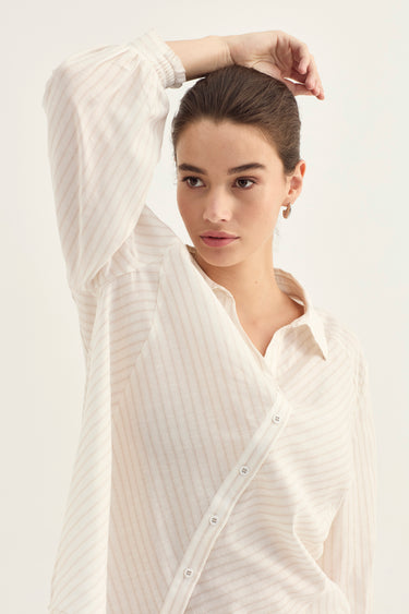 A woman wearing a cream-colored, long-sleeved button-up shirt with subtle vertical stripes by Verge, posed against a solid off-white background.