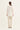 A woman viewed from the back wearing a cream-colored textured long-sleeve blouse and beige trousers by Verge, standing against a plain off-white studio background.